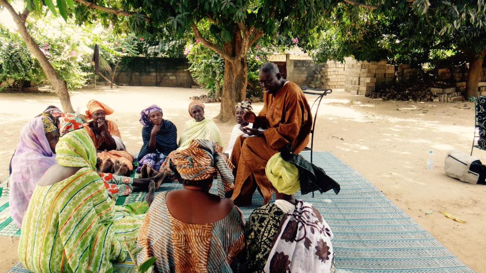 A community gathering sitting together under a tree in a rural setting